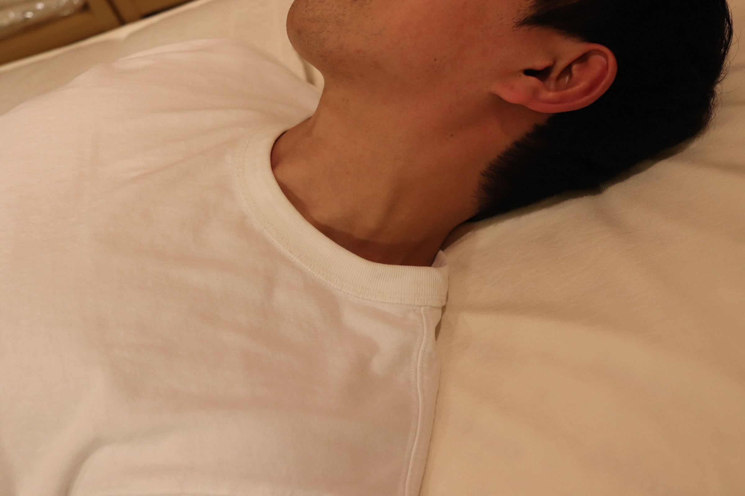 仰向けで寝て枕を使って首の力、首筋に力が入っている状態の写真